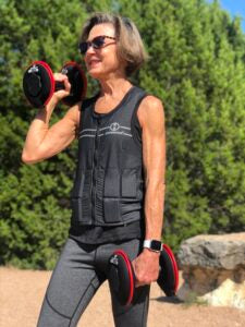 Image of woman wearing hyper vest fit weighted vest while walking with dumbbells
